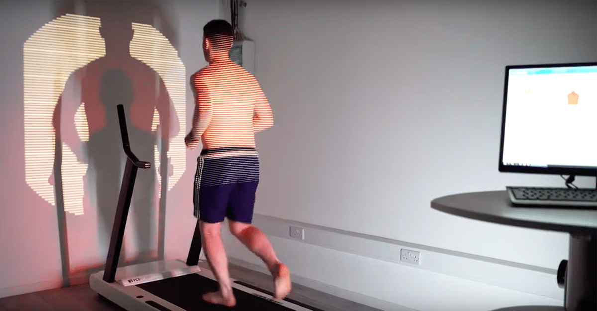 A person walking on a treadmill in a room with interesting shadow patterns on the wall, and a computer monitor displaying an FCE Scan on a desk to the right. | FCE Scan
